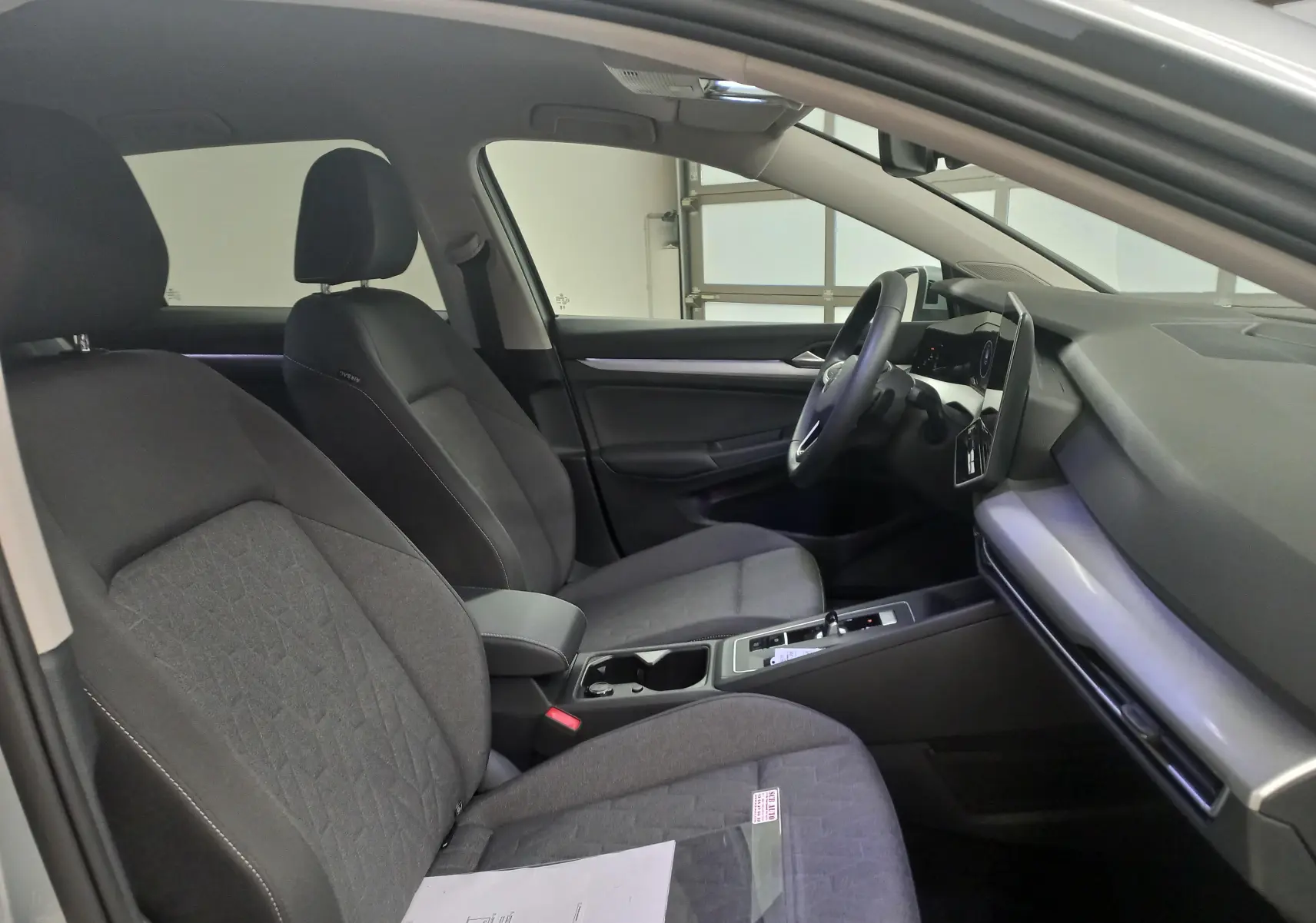 Vue intérieure côté gauche de la Volkswagen Golf 1.5 eHybrid 2025 avec sièges tissu gris et tableau de bord moderne.