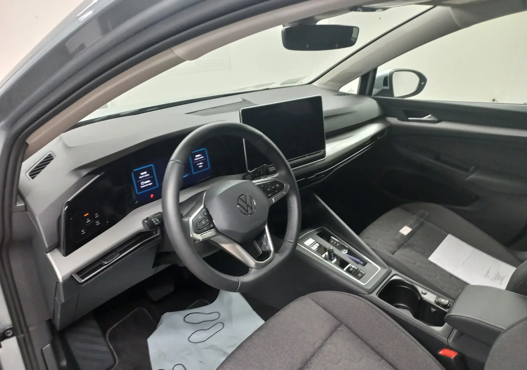 Vue intérieure côté conducteur de la Volkswagen Golf 1.5 eHybrid 2025, tableau de bord numérique et écran tactile central.