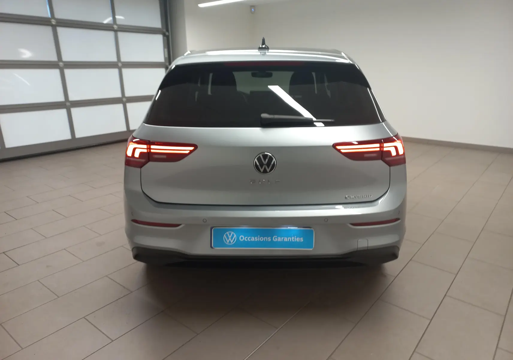 Vue arrière d'une Volkswagen Golf 1.5 eHybrid 204 DSG6 argent Dolomite avec feux LED allumés dans un intérieur neutre.