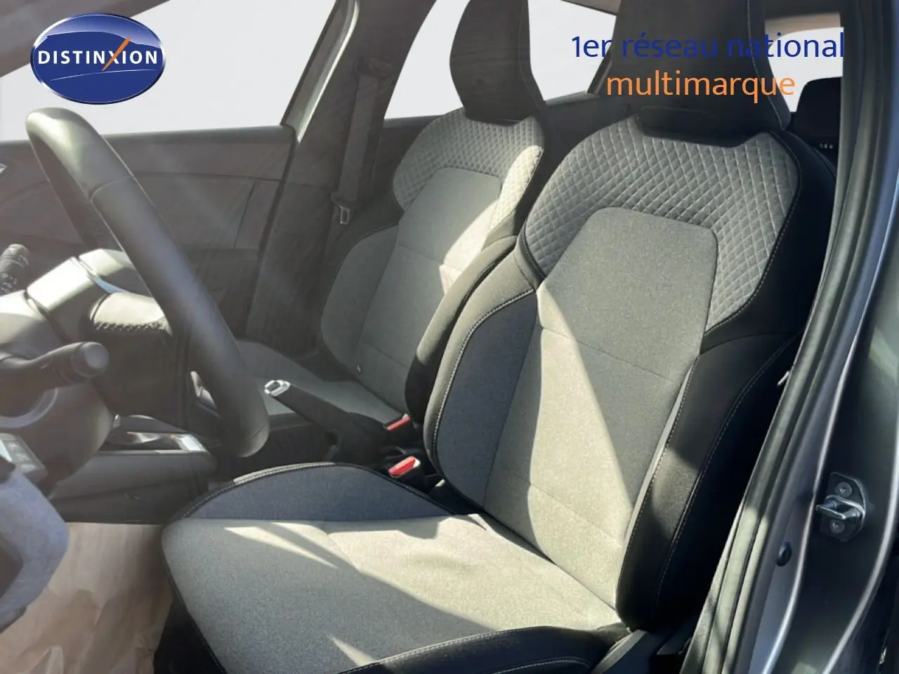 Vue intérieure côté conducteur de la Renault Clio 2025, sièges tissu gris et noir avec surpiqûres apparentes.