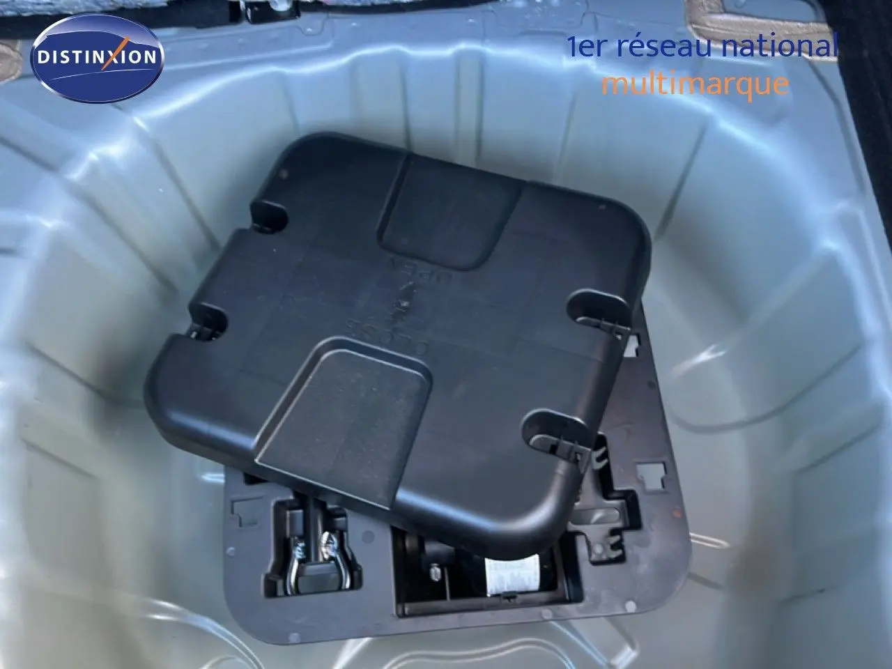 Coffre ouvert d’une Renault Clio gris schiste métal, montrant le rangement sous plancher avec kit de réparation pneus.