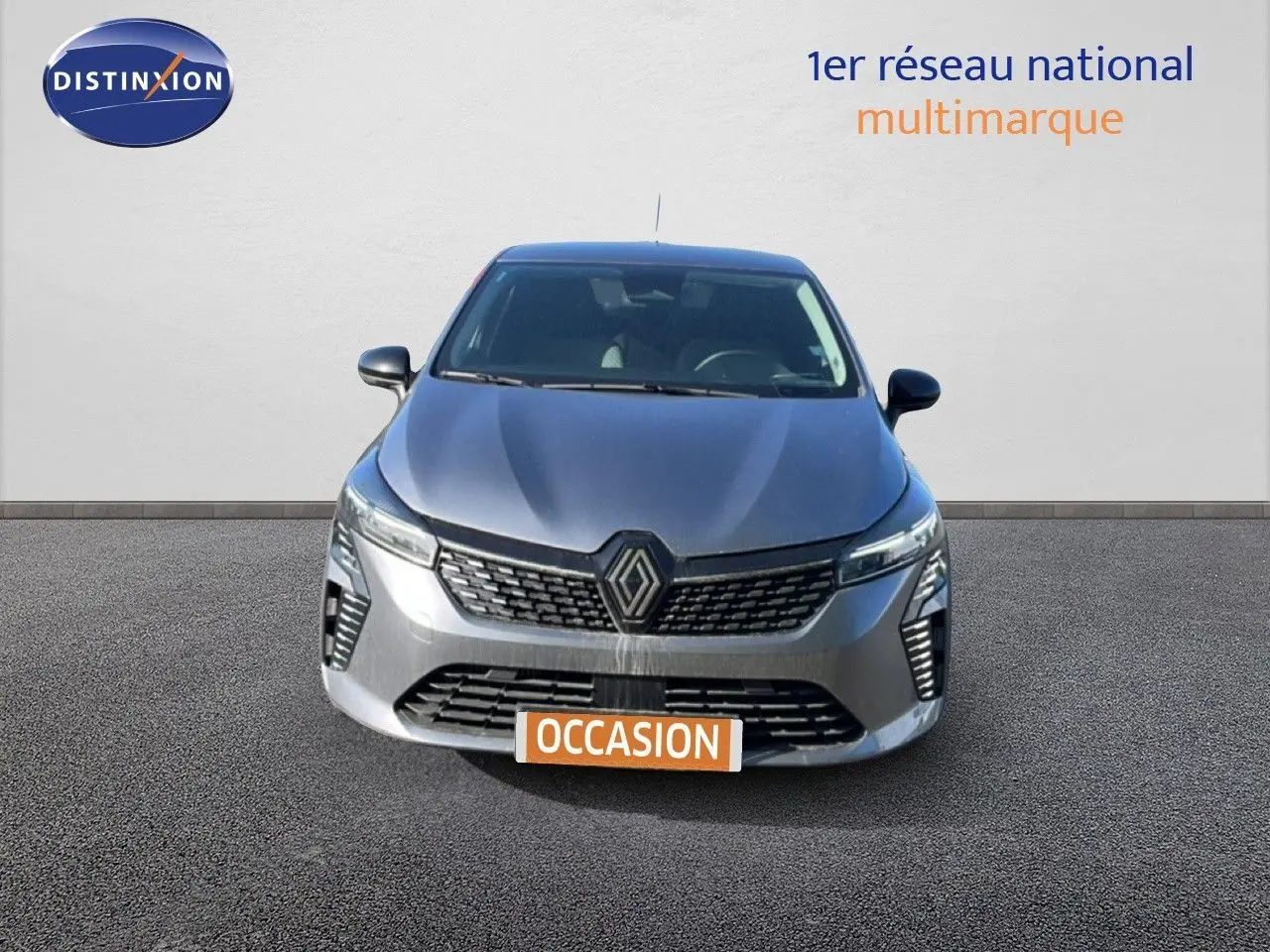 Vue frontale d'une Renault Clio gris schiste métal 2025 avec calandre moderne et phares LED allumés.