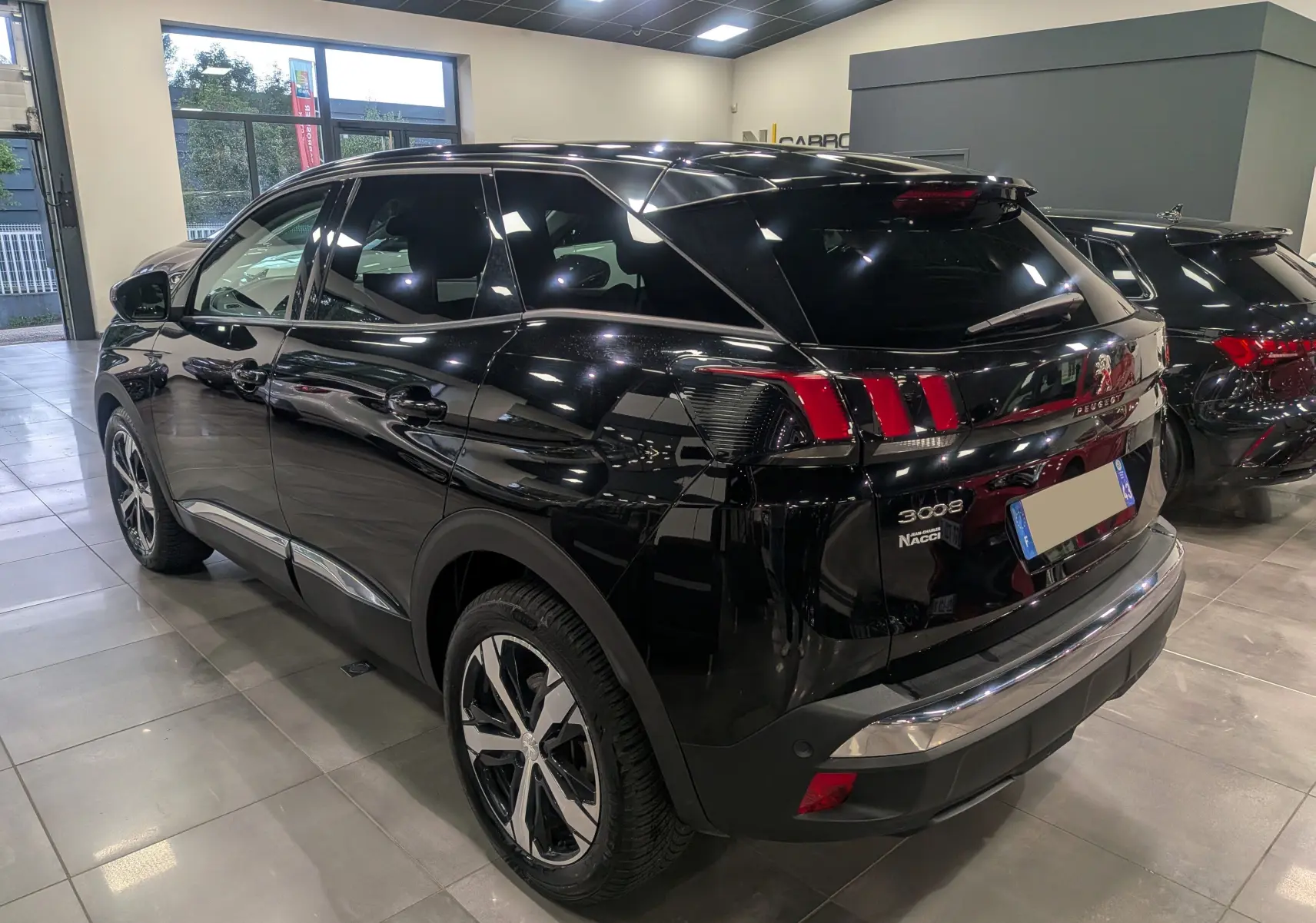 Vue 3/4 arrière droite du Peugeot 3008 noir Perla avec feux arrière à griffes et jantes bi-ton en showroom.
