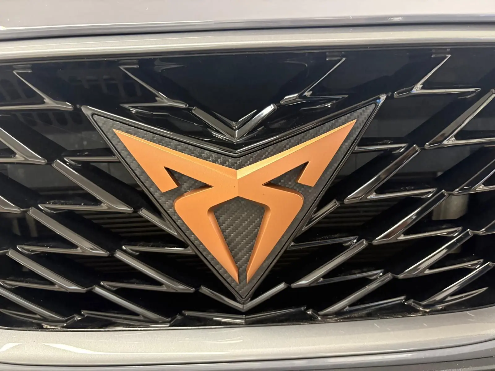 Gros plan sur la calandre noire avec le logo CUPRA cuivré, entourée de la carrosserie gris graphène.