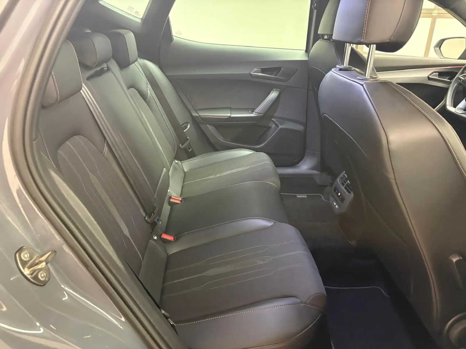 Vue intérieure côté arrière gauche du CUPRA Formentor gris Graphène, montrant les sièges arrière en cuir avec surpiqûres contrastées.