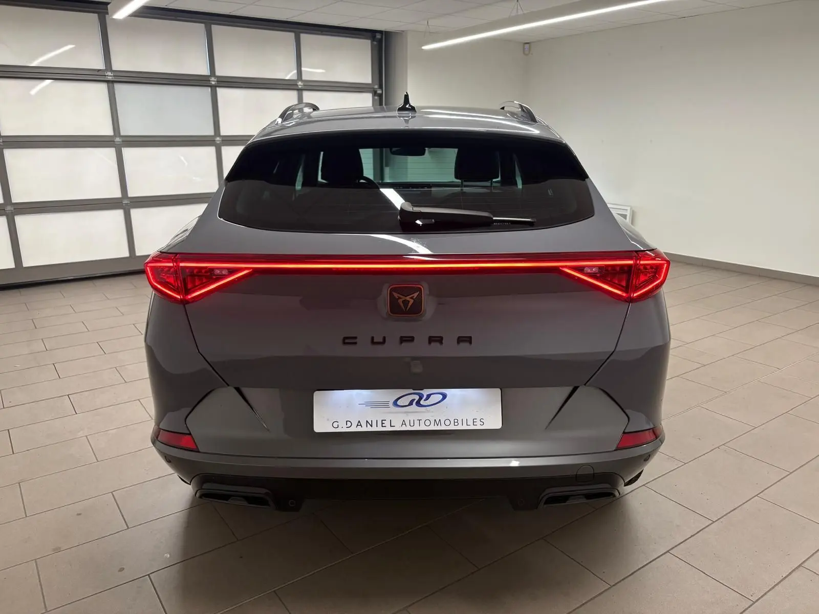 Vue arrière d'une CUPRA Formentor gris Graphène 2022 avec feux arrière allumés et hayon électrique en intérieur.