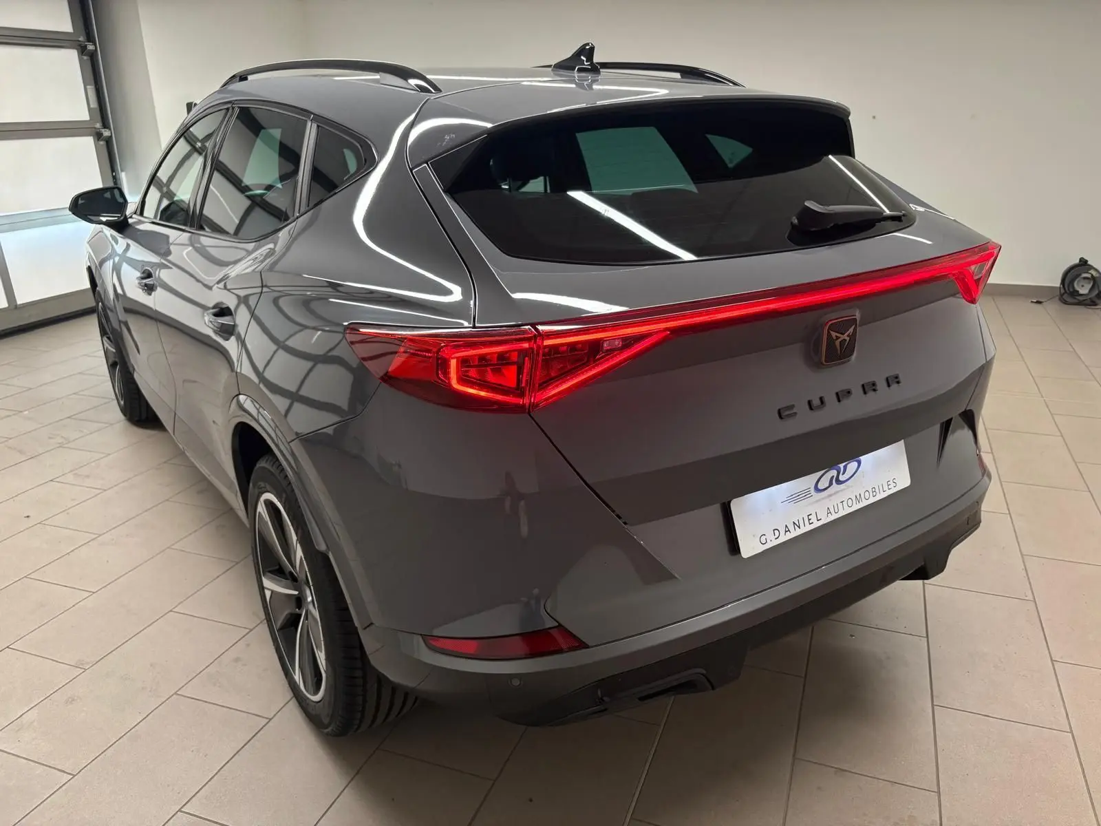 Vue 3/4 arrière droite du CUPRA Formentor gris Graphène avec feux arrière allumés et jantes 18 pouces en alliage.