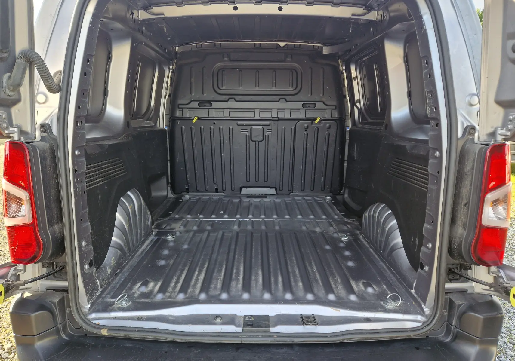 Vue arrière ouverte du fourgon Peugeot Partner gris Artense, montrant l'espace de chargement vide et les feux arrière rouges.