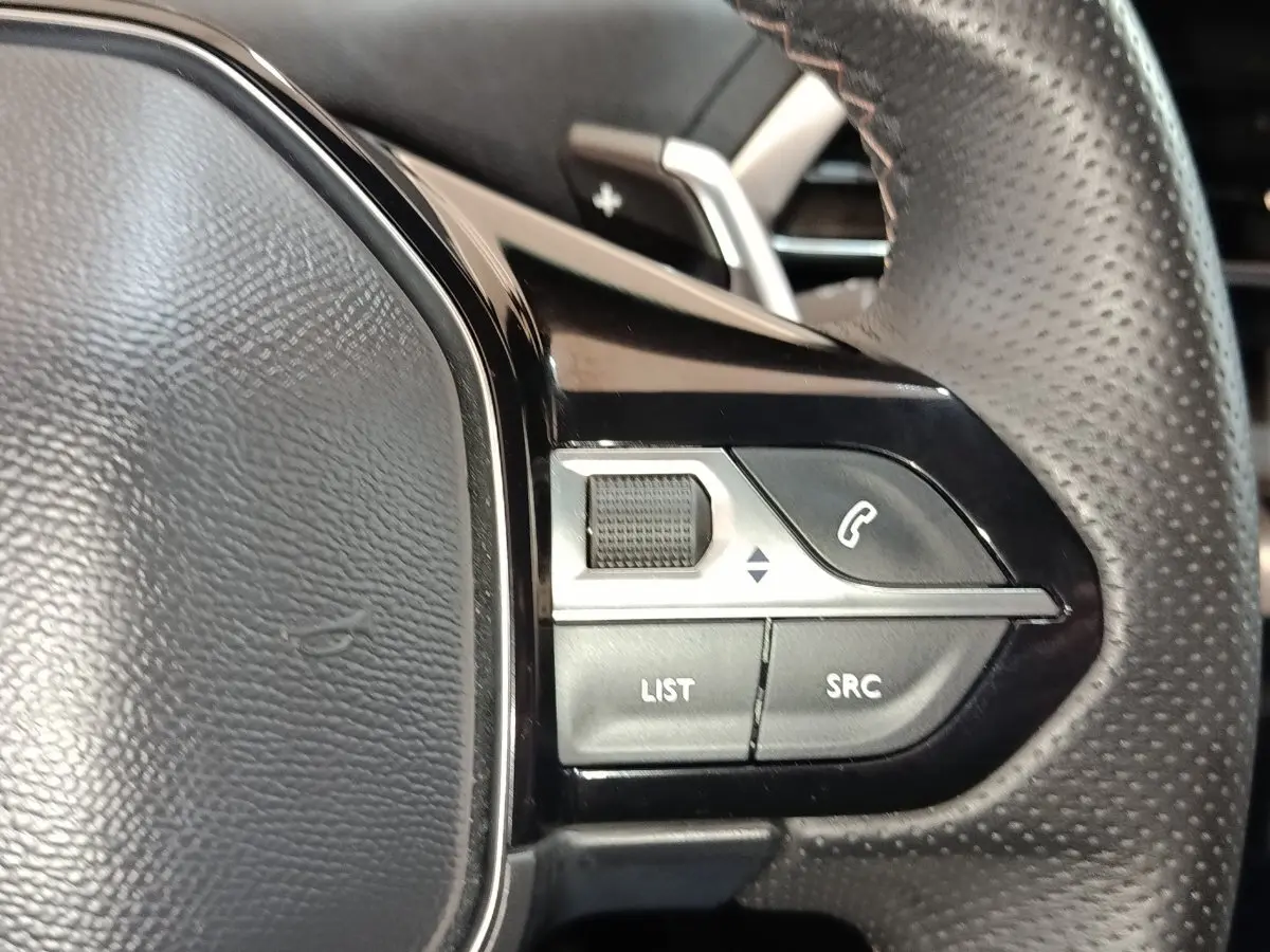 Gros plan sur les commandes gauche du volant en cuir perforé du Peugeot 5008 bleu, boutons multifonctions visibles.