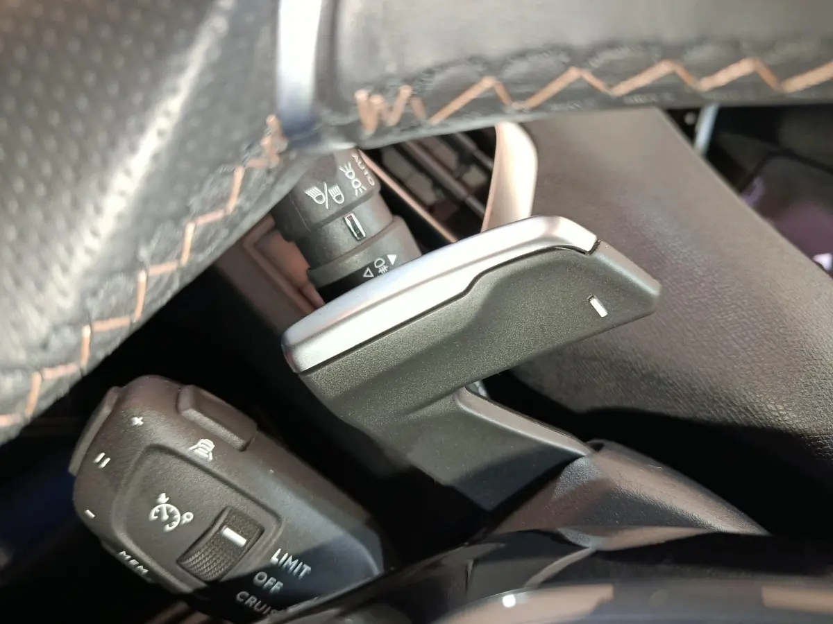 Gros plan sur la commande de régulateur de vitesse et palettes au volant cuir noir du Peugeot 5008 GT bleu 2023.