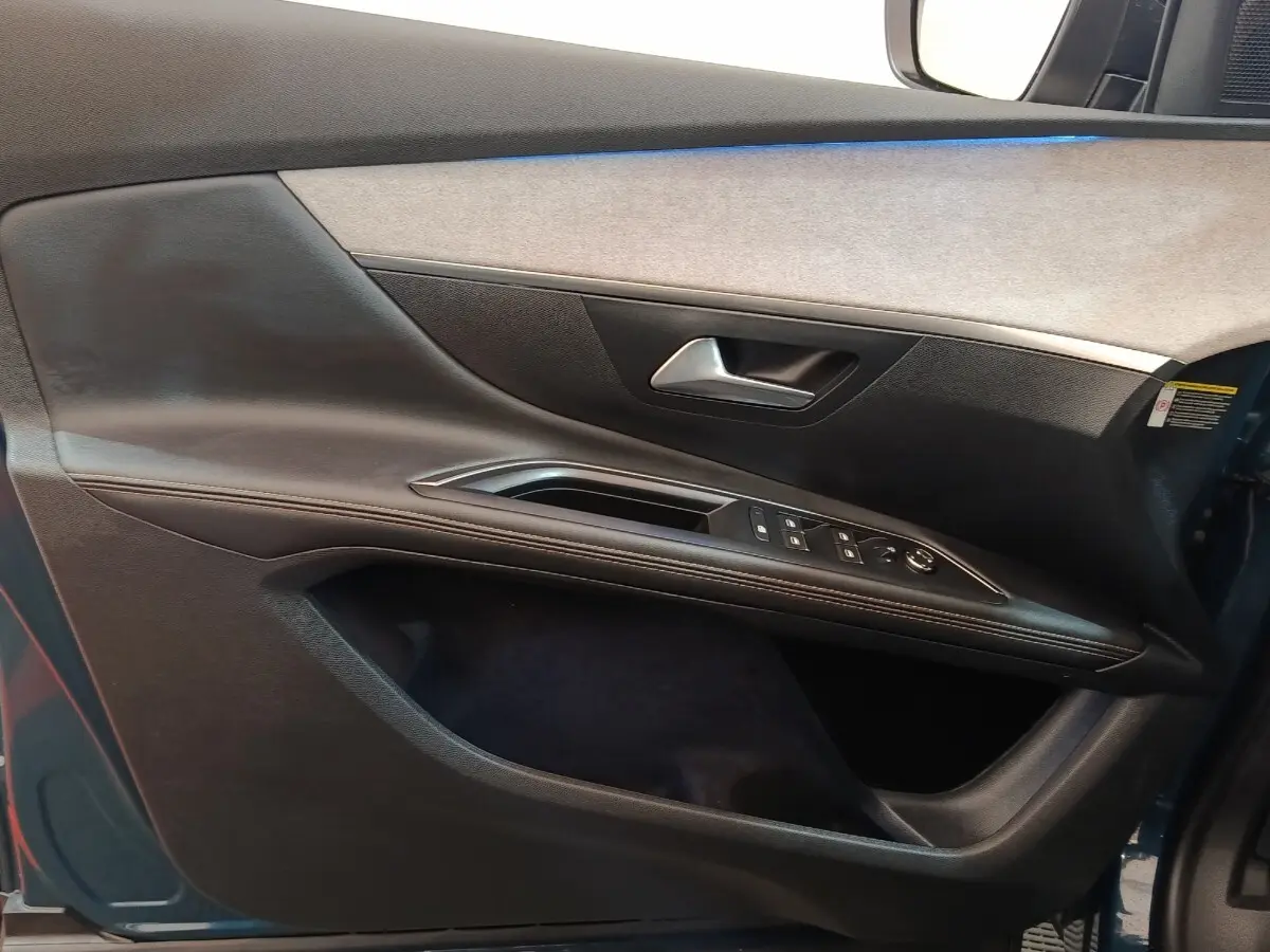 Vue rapprochée de la porte avant gauche du Peugeot 5008 bleu 2023, avec commandes de vitres et poignée argentée.
