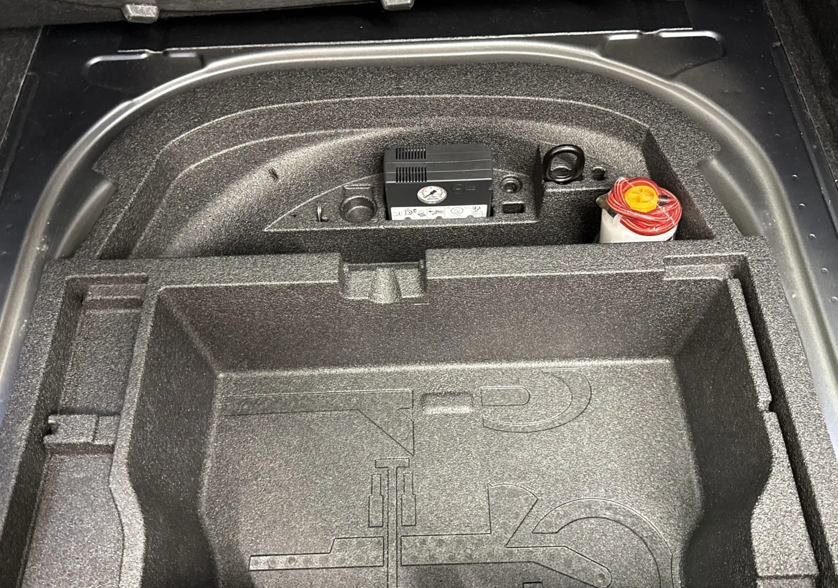 Compartiment de rangement sous le plancher du coffre de la Skoda Octavia Combi gris graphite 2023, avec kit de réparation pneus visible.