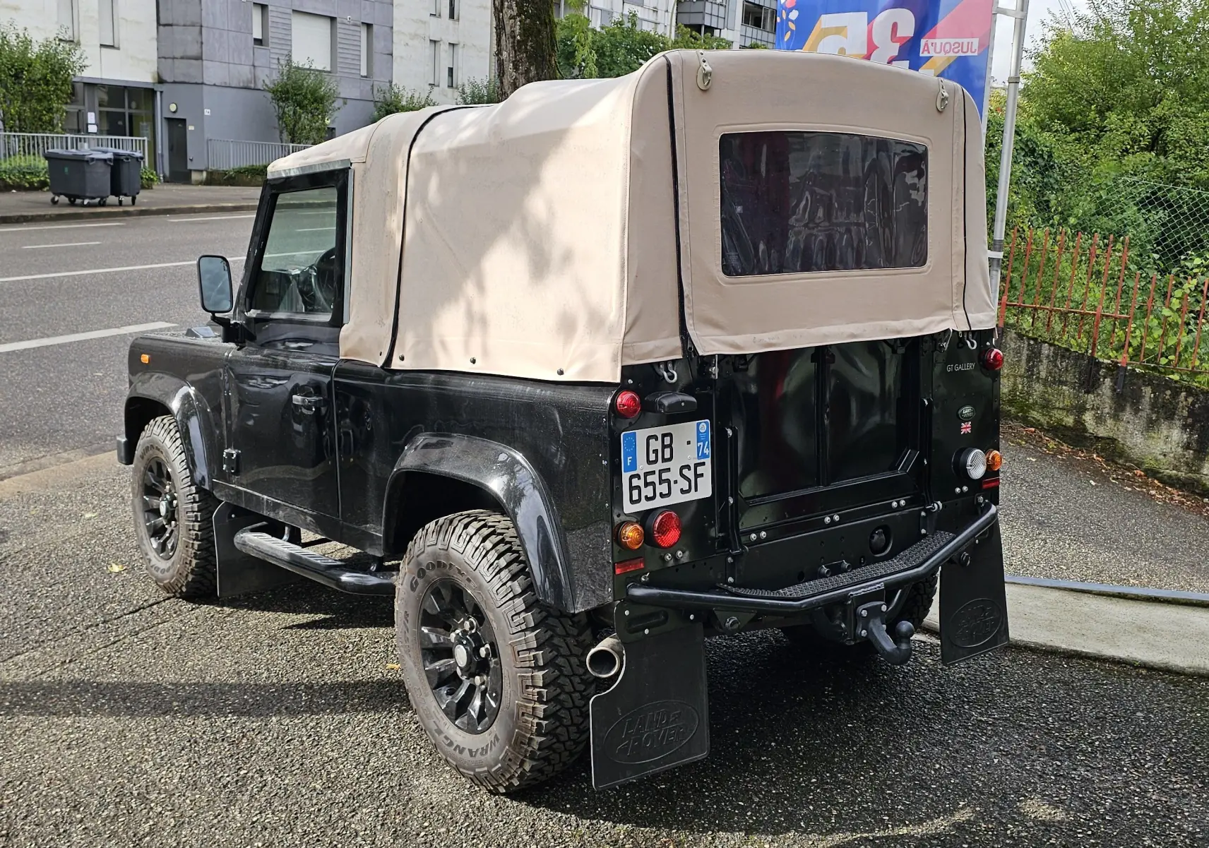 Land Rover 90 Defender noir vu en 3/4 arrière droit avec capote souple beige et roues tout-terrain.