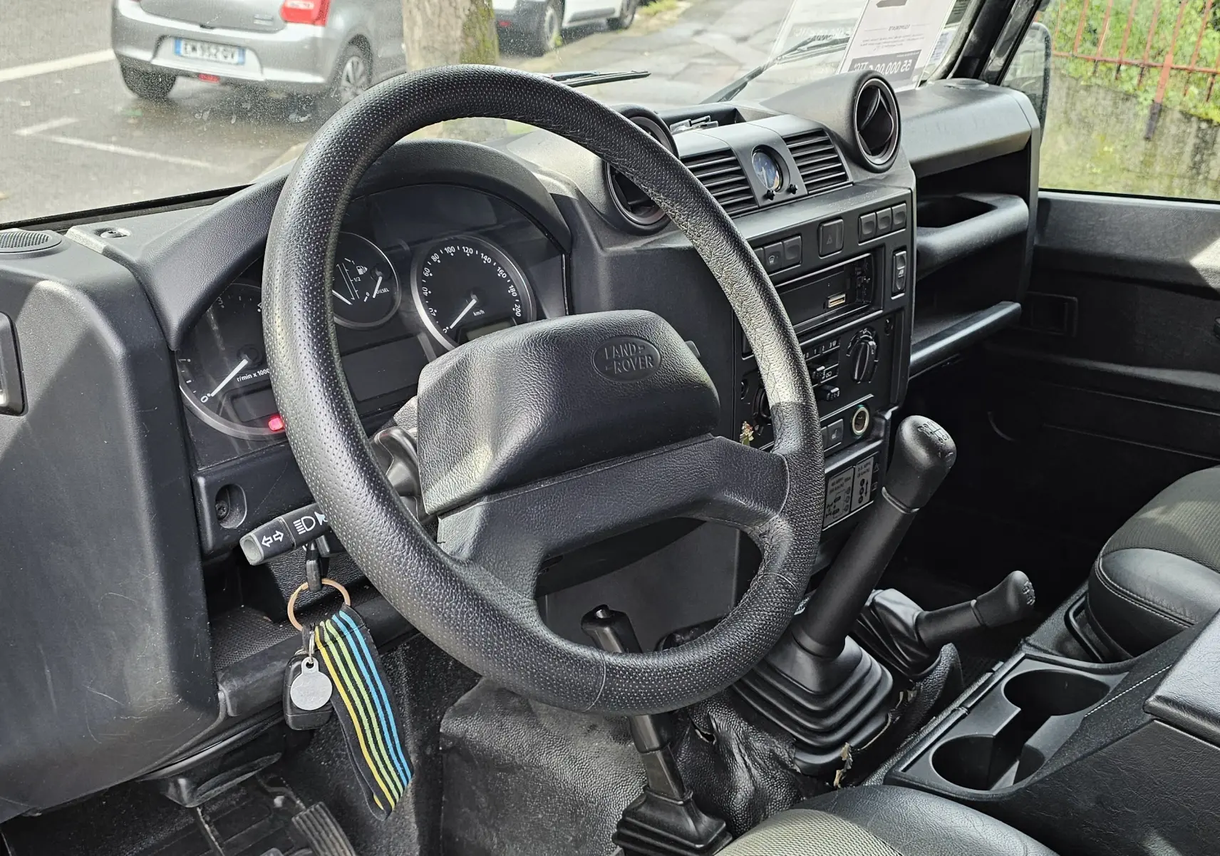 Intérieur noir du Land Rover Defender 90 2013, vue côté conducteur sur le volant, levier de vitesses manuel et tableau de bord.