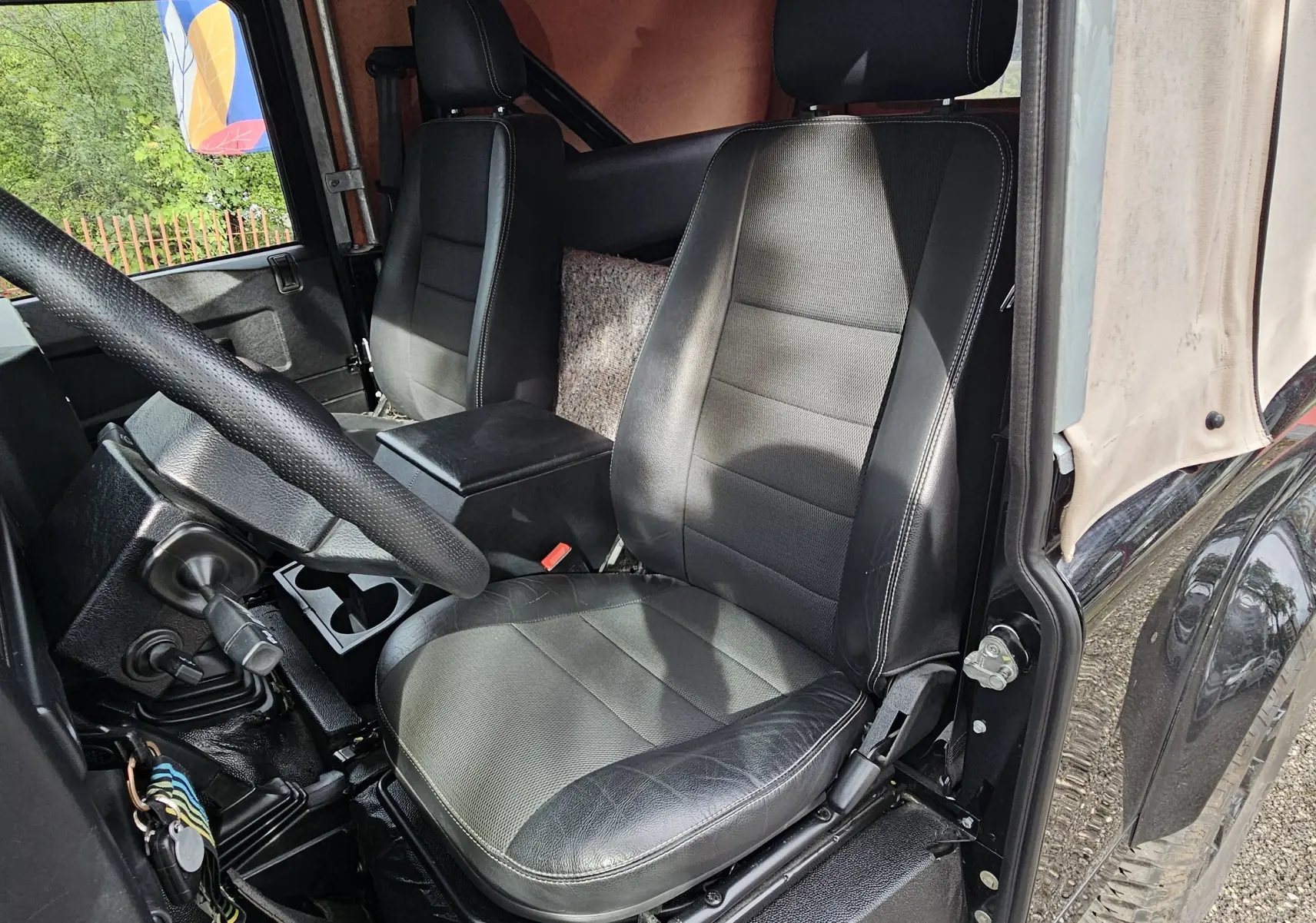 Vue intérieure côté conducteur du Land Rover Defender 90 noir avec sièges en cuir et capote beige souple.