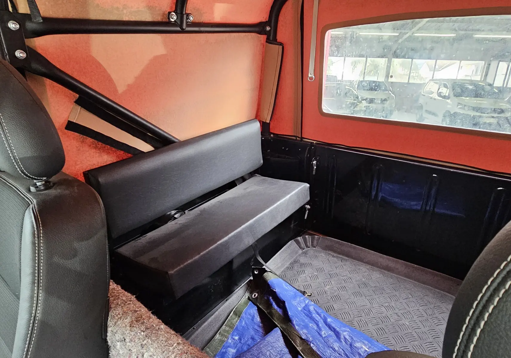 Vue intérieure arrière du Land Rover Defender 90 noir avec banquette latérale et fenêtre arrière visible dans un garage.