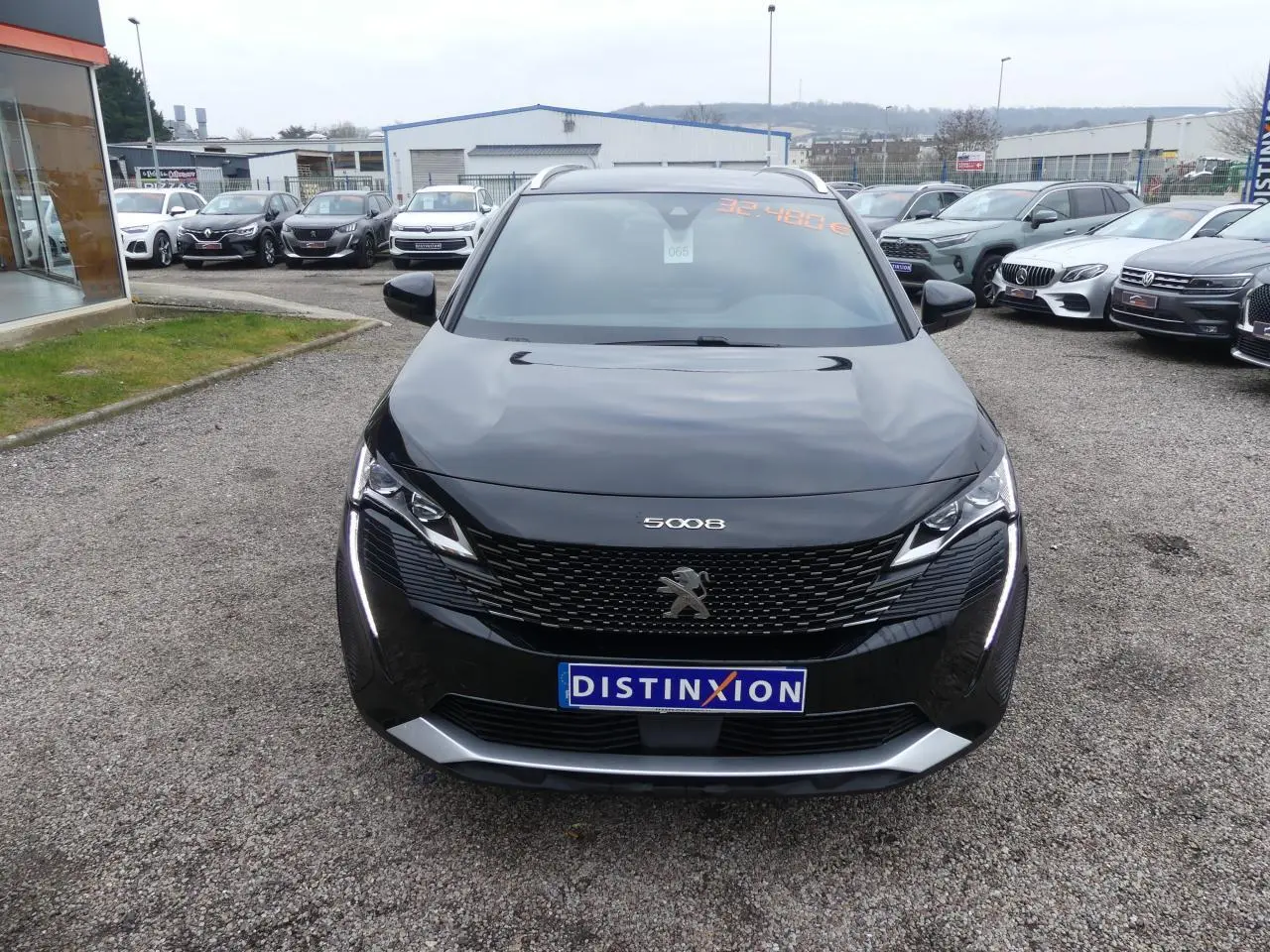 Vue frontale d'un Peugeot 5008 noir métallisé avec calandre GT et feux LED verticaux allumés sur un parking.