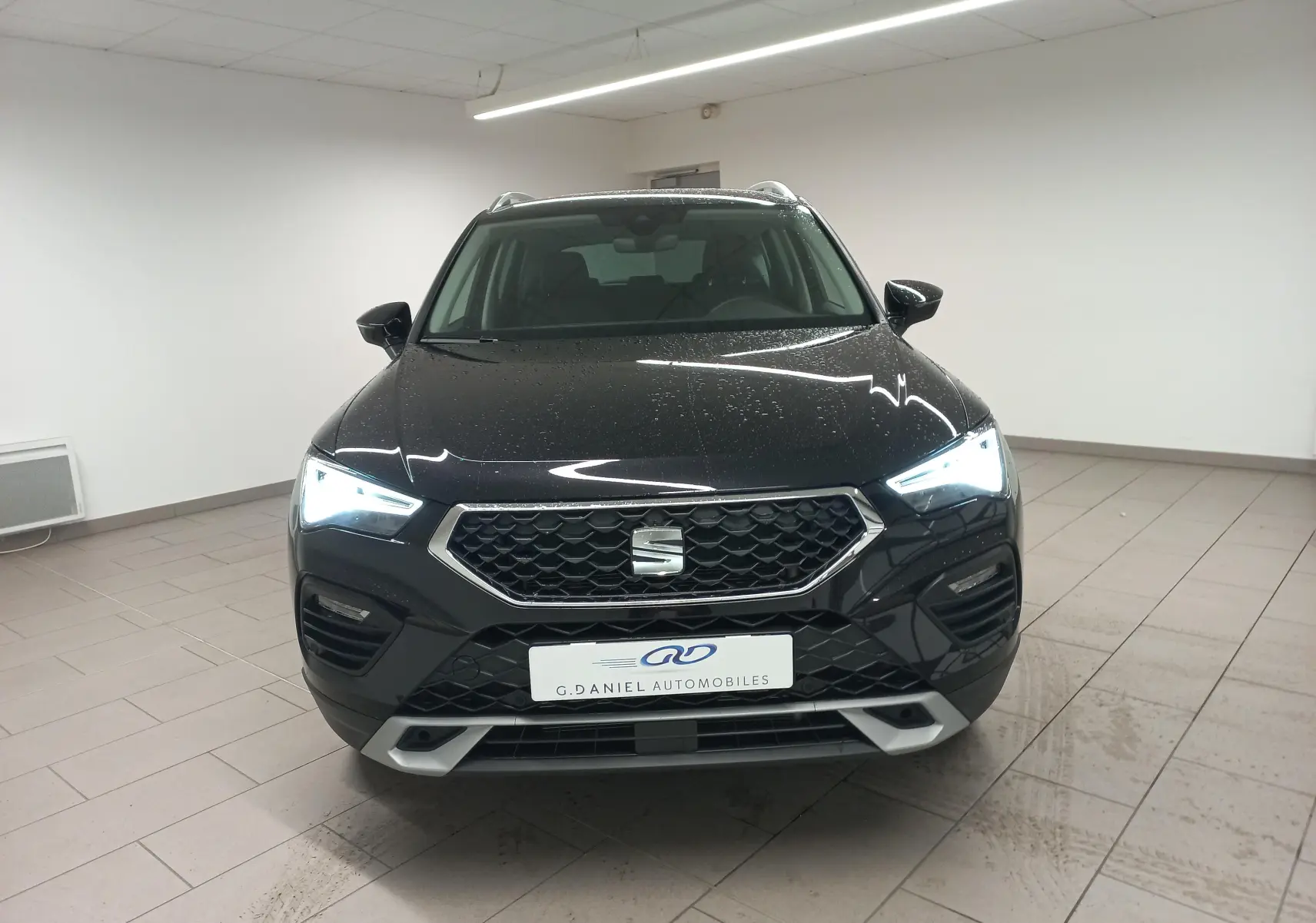 Vue avant d'un SEAT Ateca 2.0 TDI 150 DSG7 Copa noir Magic Nacré avec phares allumés dans un showroom.