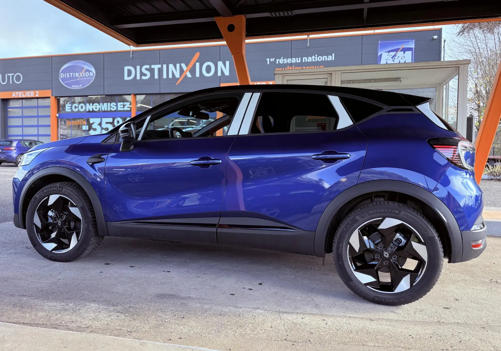 Profil côté gauche du Renault Captur E-Tech F.Hybrid 145ch 2025 en bleu Iron Metal avec toit noir et jantes noires distinctives.