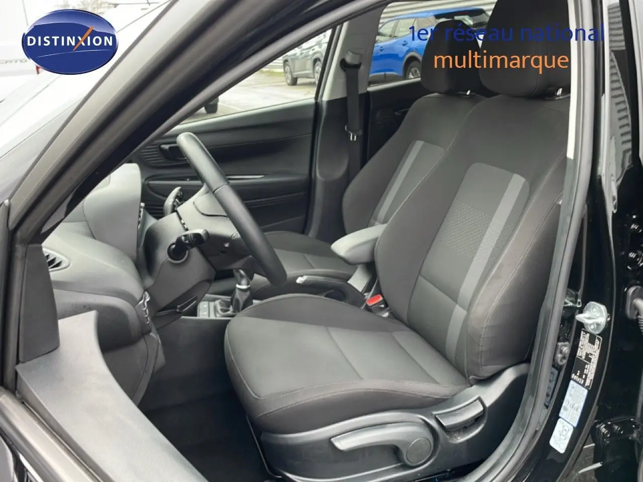 Intérieur côté conducteur d'une Hyundai i20 noire, montrant les sièges en tissu gris et le volant multifonction.