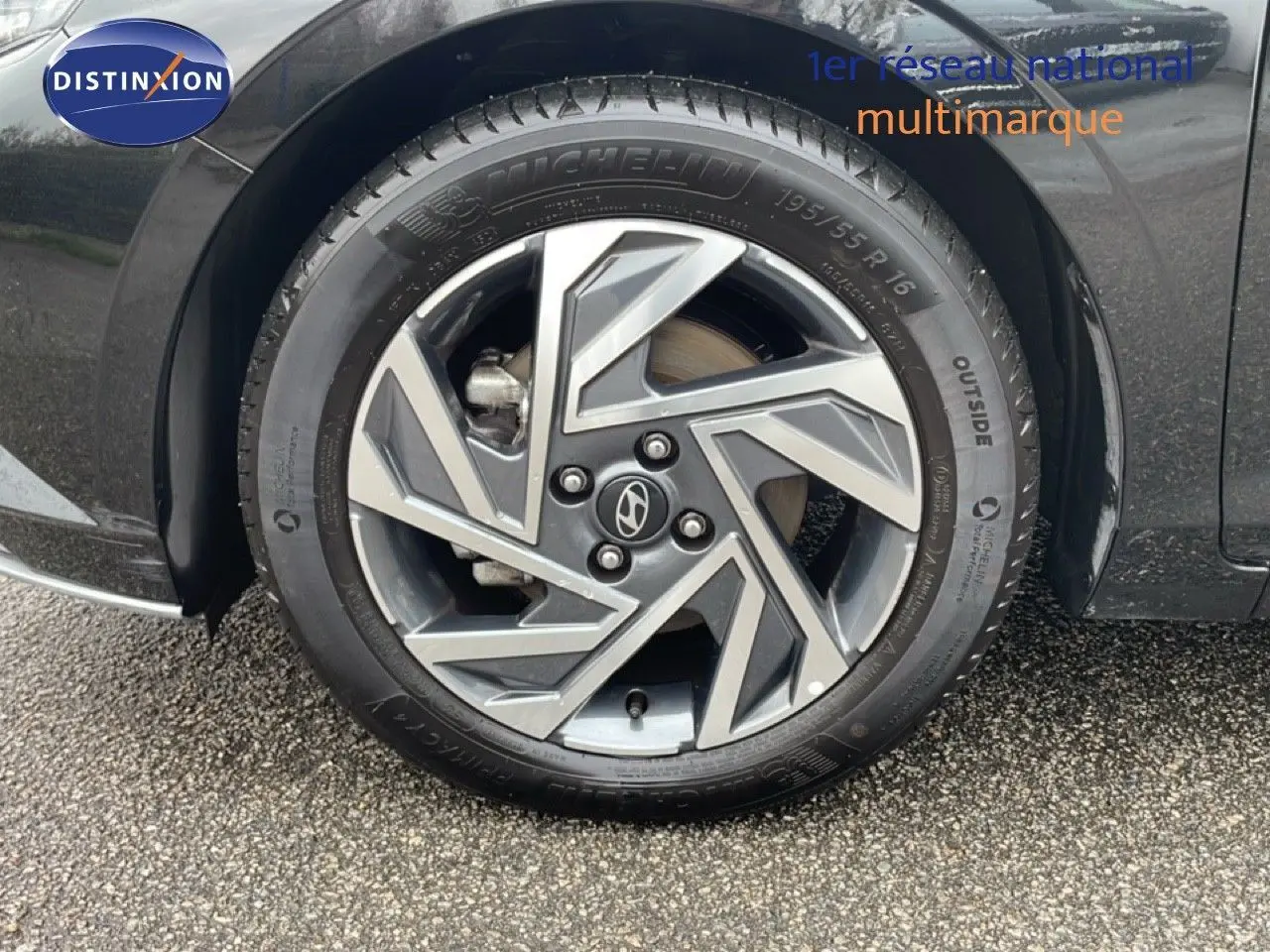 Gros plan sur la roue avant droite d'une Hyundai i20 noire Phantom Metal avec jante alliage au design géométrique.