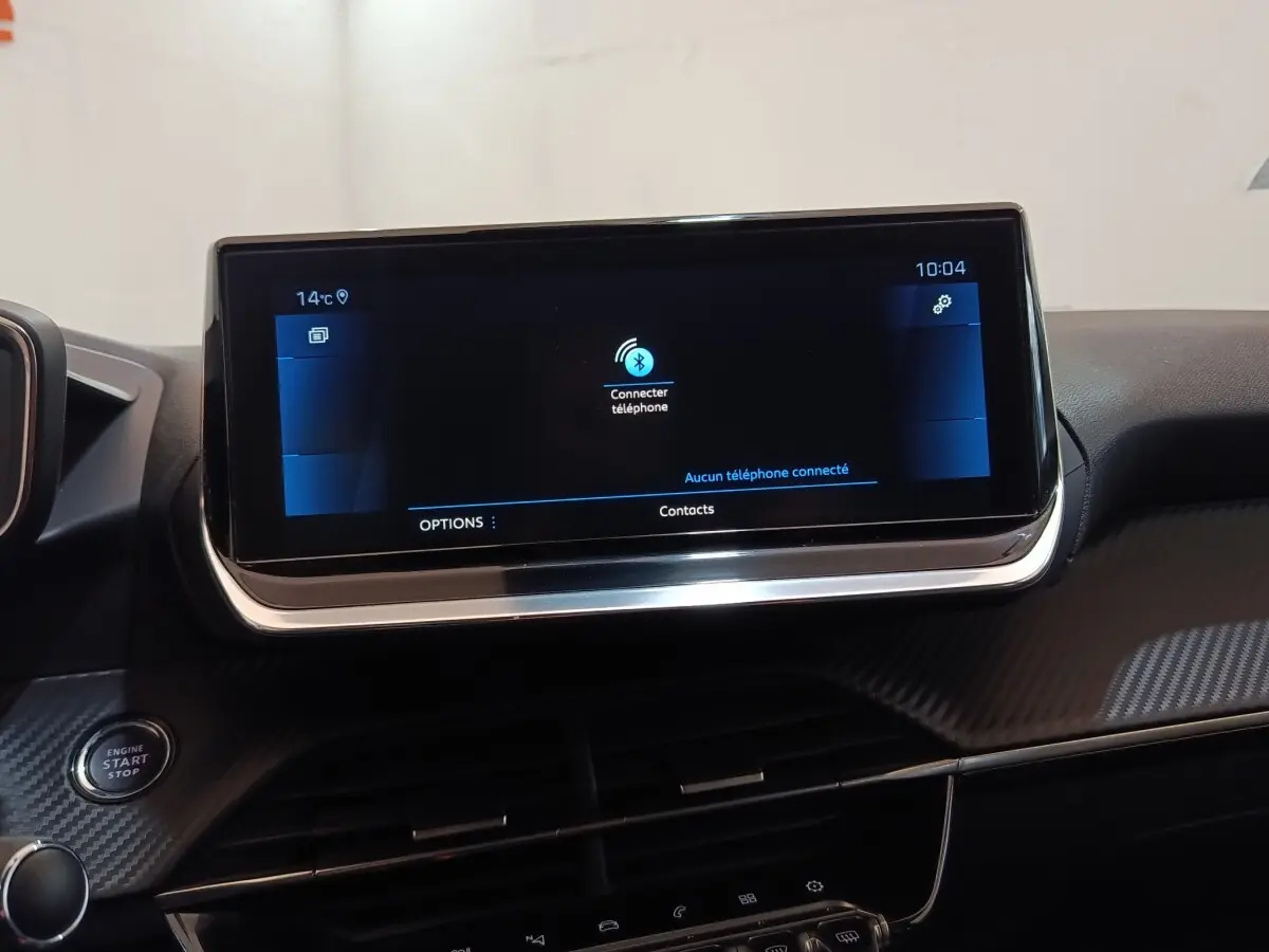 Écran tactile central allumé vu de face dans l’habitacle noir d’une Peugeot 208 blanche PureTech 2021.