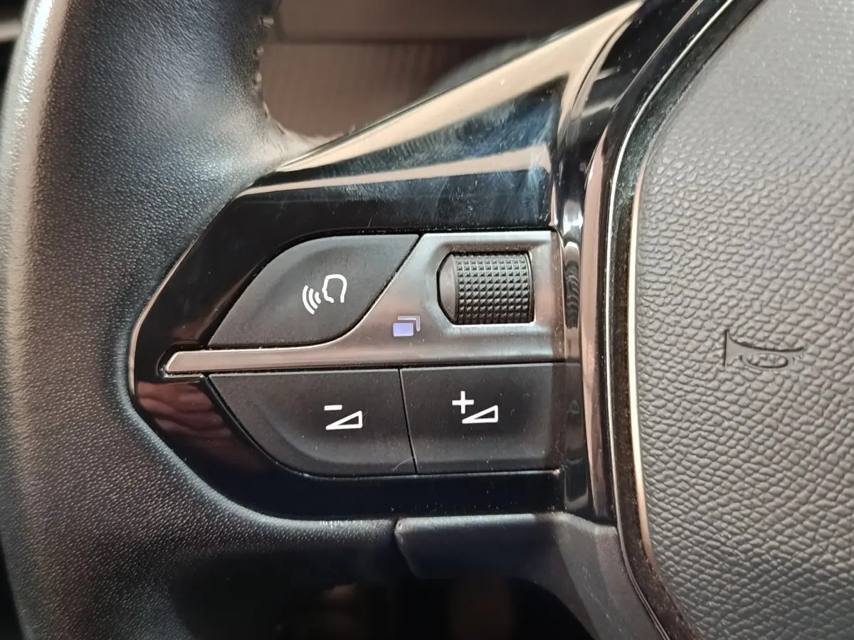 Gros plan sur les commandes gauche du volant noir de la Peugeot 208 PureTech 100 S&S Allure Business 2021.