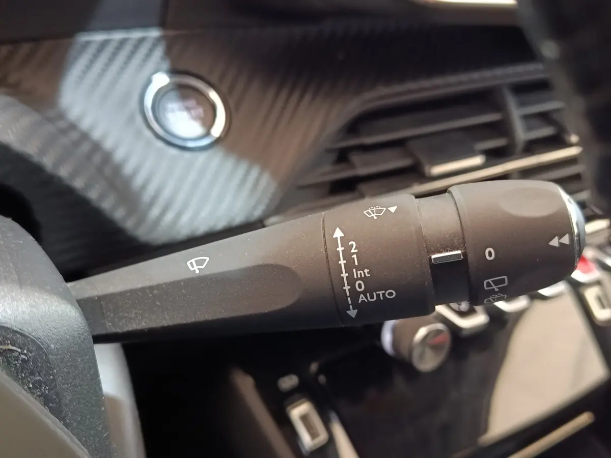 Gros plan sur la commande des essuie-glaces dans l’habitacle du Peugeot 208 blanc, avec bouton démarrage en arrière-plan.