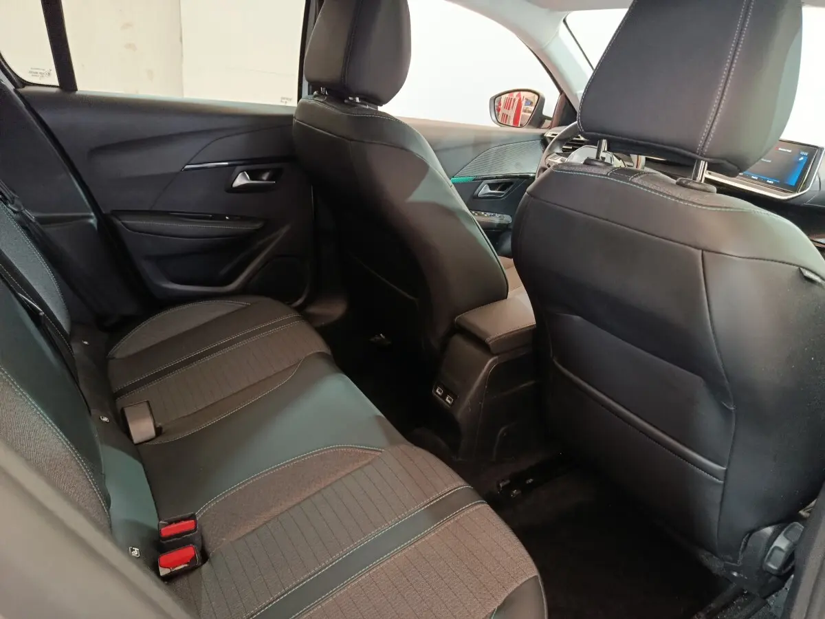 Vue intérieure arrière côté gauche de la Peugeot 208 blanche, montrant la banquette et les sièges avant en cuir noir.