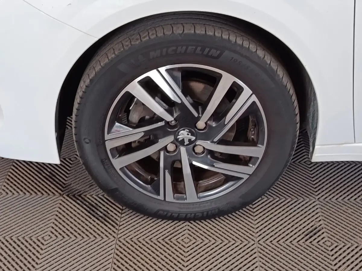 Gros plan sur la roue arrière droite d'une Peugeot 208 blanche avec jante alliage et logo lion au centre.