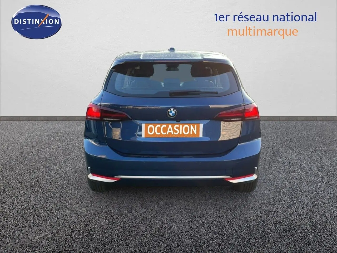 Vue arrière d'une BMW Série 2 Active Tourer 218i bleu phytonique métallisé avec feux arrière allumés sur fond neutre.