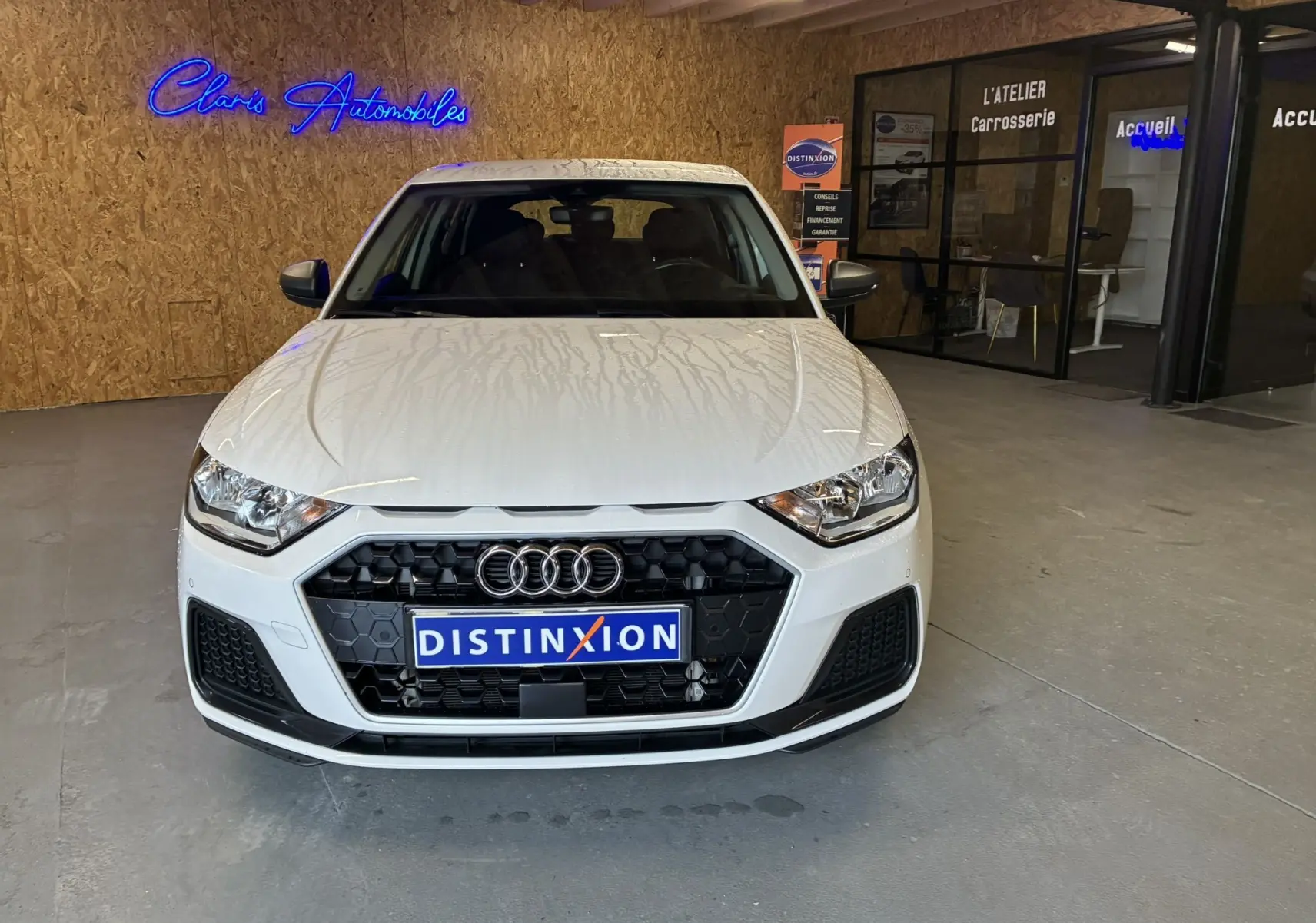 Audi A1 blanche vue de face en intérieur, avec calandre noire hexagonale et logo Audi bien visible.