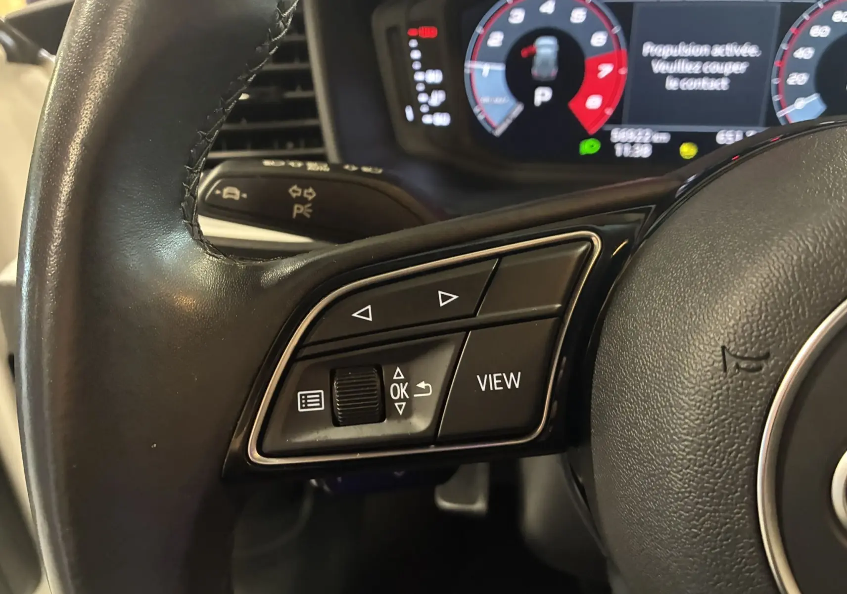 Gros plan sur les commandes gauche du volant cuir noir d’une Audi A1 blanche, avec affichage numérique en arrière-plan.