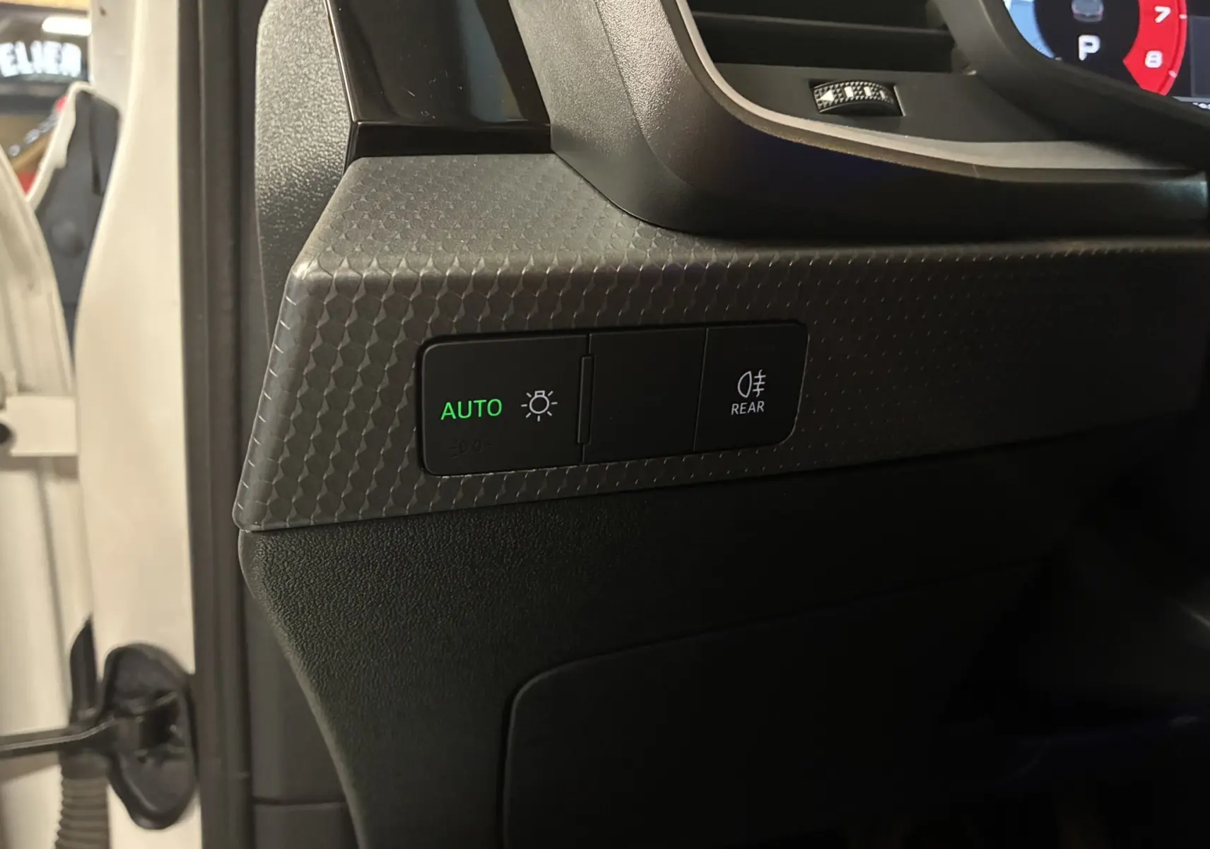 Détail intérieur du tableau de bord côté gauche d’une Audi A1 blanche 2022 avec commande d’éclairage automatique et antibrouillard arrière.