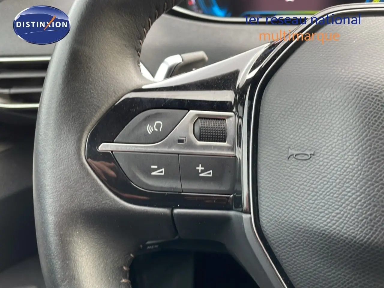 Gros plan sur la partie gauche du volant noir du Peugeot 3008 hybride 2024, avec commandes audio et bouton de volume.