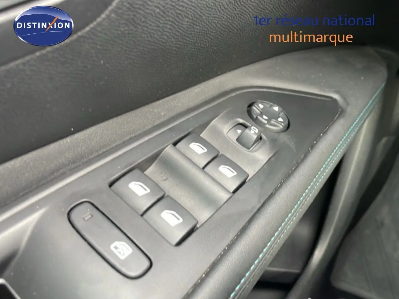 Gros plan sur les commandes des vitres et rétroviseurs côté conducteur, avec surpiqûres bleues sur la garniture noire.