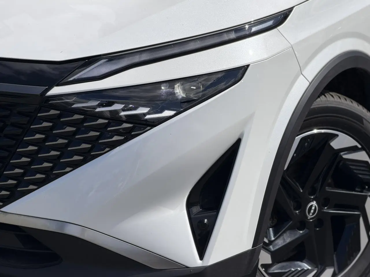 Gros plan sur l'avant droit du Nissan Qashqai blanc nacré avec calandre noire et jante alliage 18 pouces.