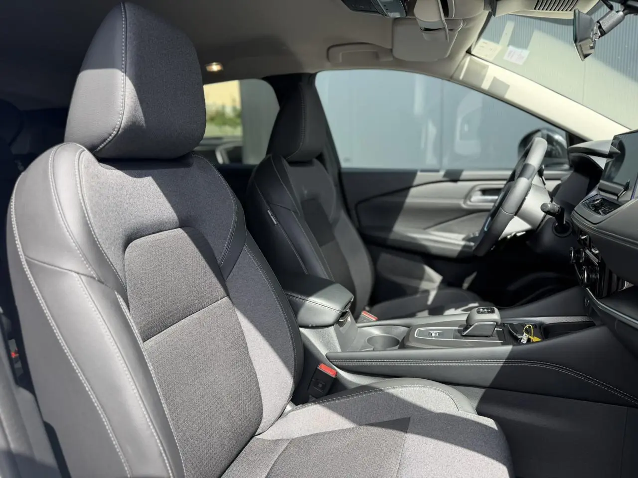 Vue intérieure côté gauche du Nissan Qashqai 2025, sièges avant en tissu et TEP noir avec surpiqûres blanches.