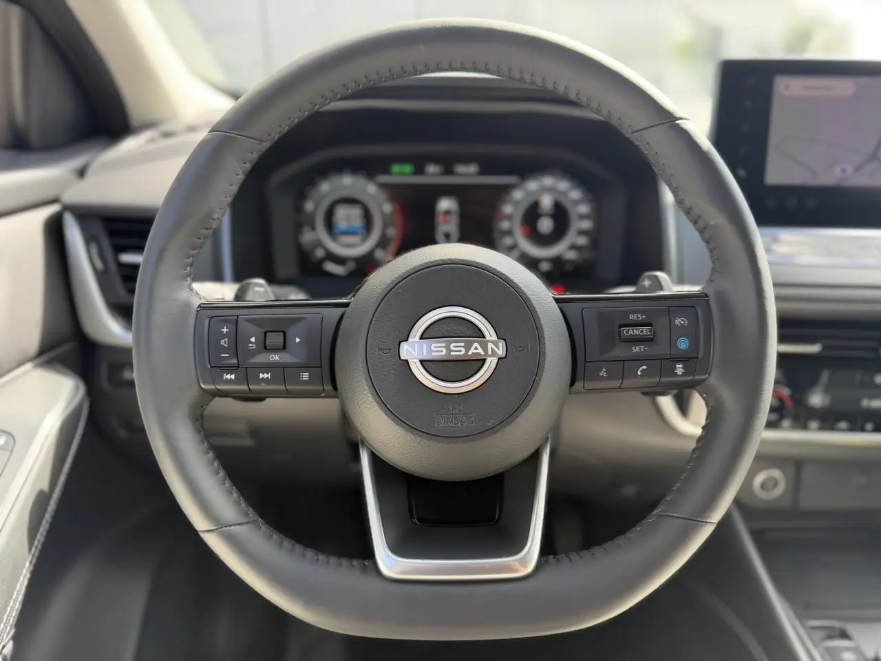 Vue rapprochée du volant cuir noir du Nissan Qashqai 2025 avec commandes intégrées et tableau de bord numérique flou.