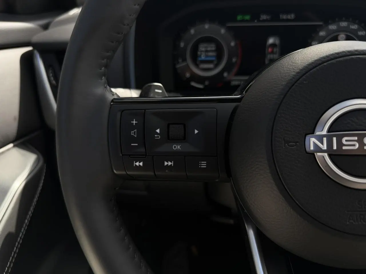 Gros plan sur le volant cuir noir du Nissan Qashqai 2025 avec commandes audio et affichage numérique en arrière-plan flou.