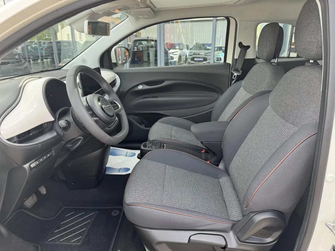 Vue intérieure côté conducteur de la Fiat 500 électrique blanche 2022 avec sellerie gris anthracite et planche de bord blanche.