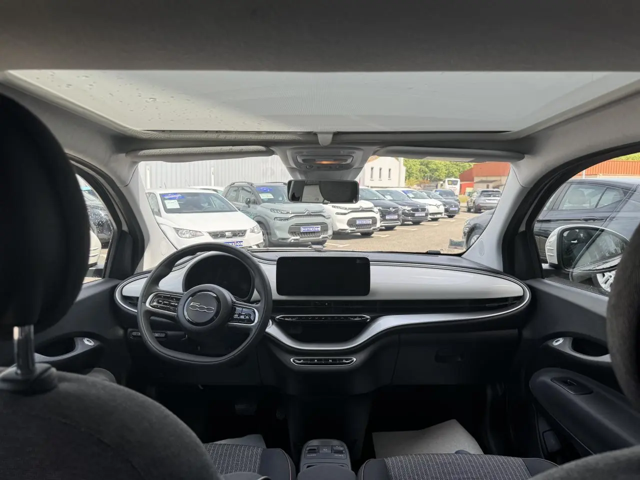 Intérieur de la Fiat 500 électrique 2022 vu de l'arrière, tableau de bord blanc avec toit panoramique et sellerie gris anthracite.