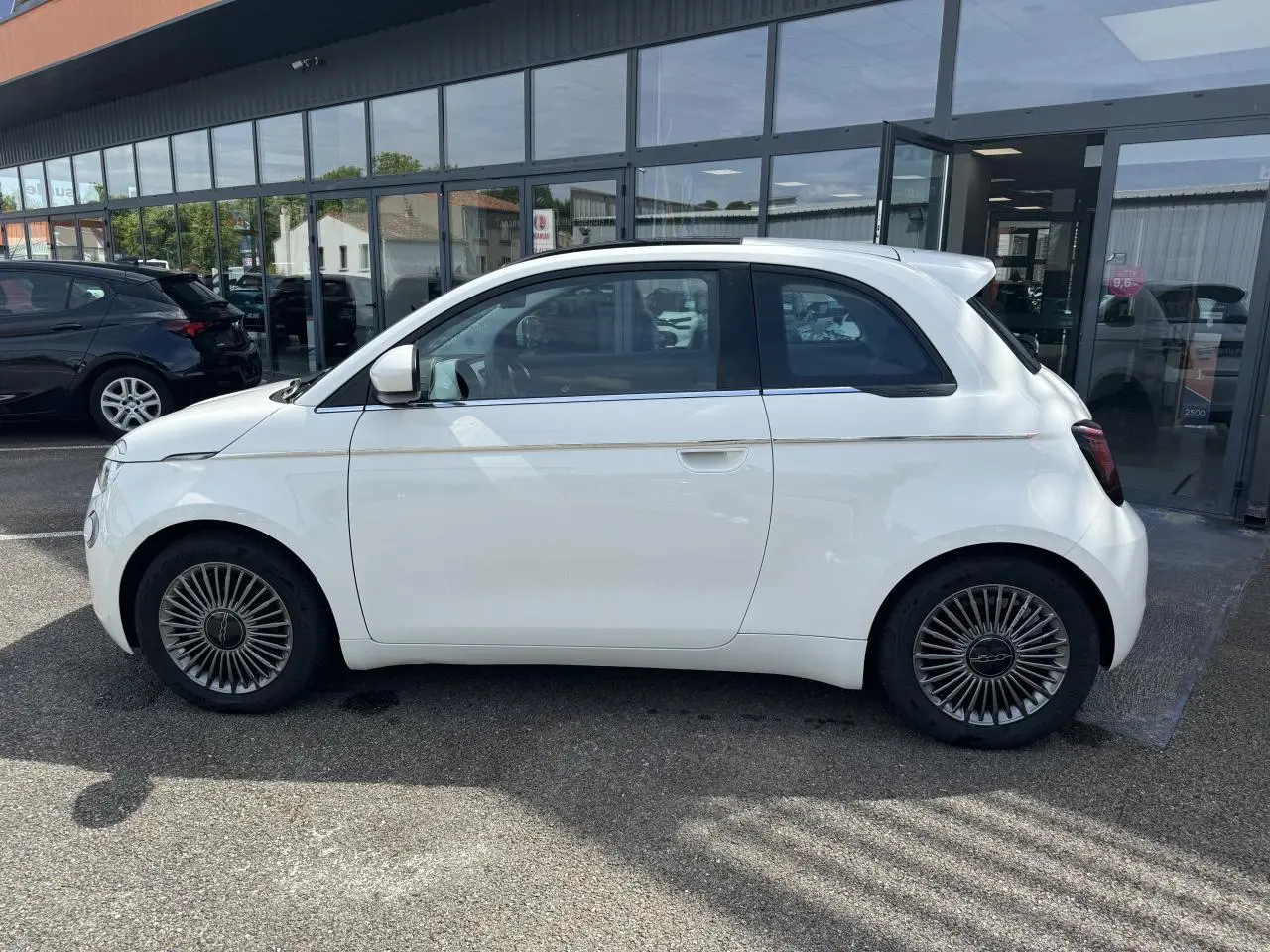 Profil côté gauche d'une Fiat 500 électrique blanche 2022 avec jantes alliage 16 pouces et toit panoramique.