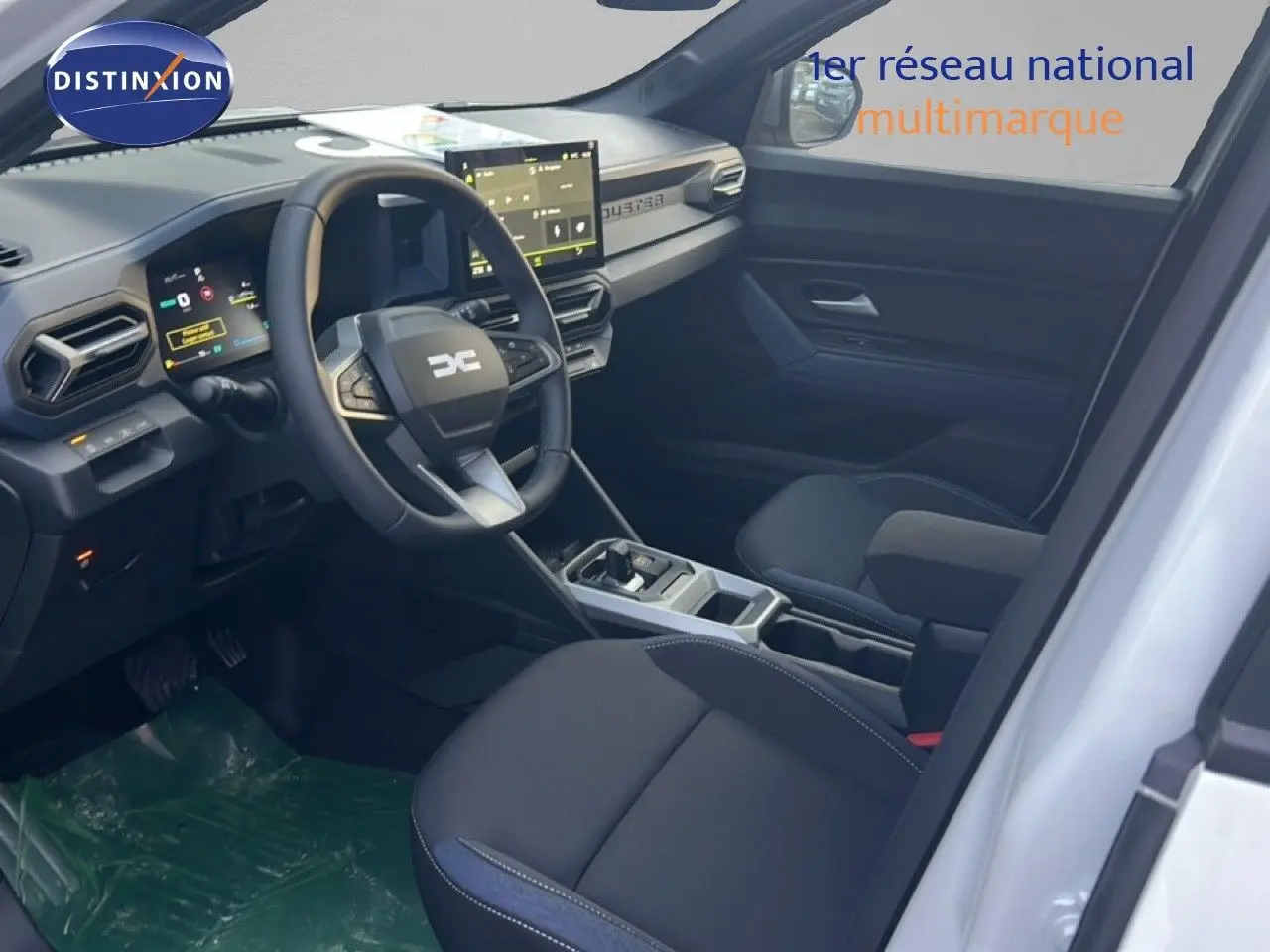 Vue intérieure côté conducteur du Dacia Duster Hybrid 140 Journey blanc Glacier, avec tableau de bord numérique et sellerie Denim.