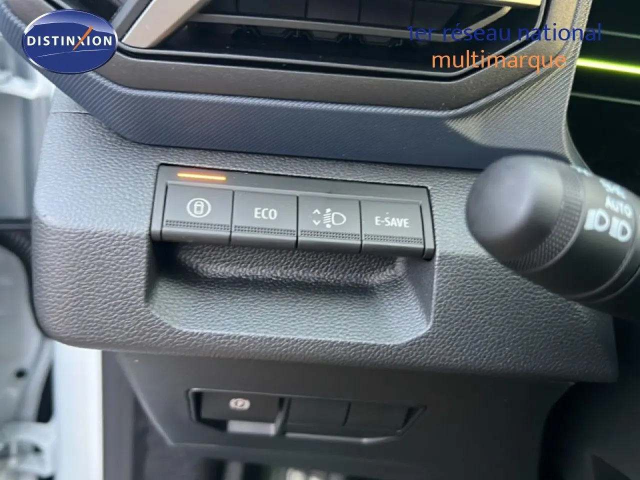 Gros plan sur les commandes de mode de conduite et feux du Dacia Duster Hybrid 140 blanc Glacier, côté gauche du tableau de bord.