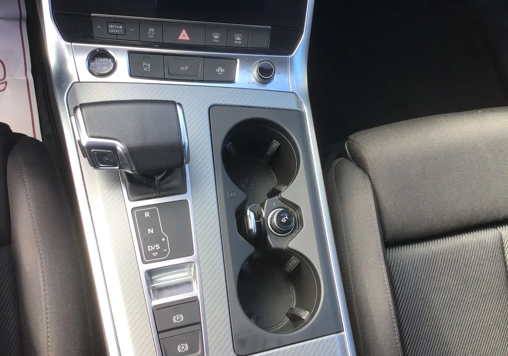 Vue rapprochée de la console centrale de l’Audi A6 Avant blanc glacier 2022, avec levier de vitesse automatique et porte-gobelets.