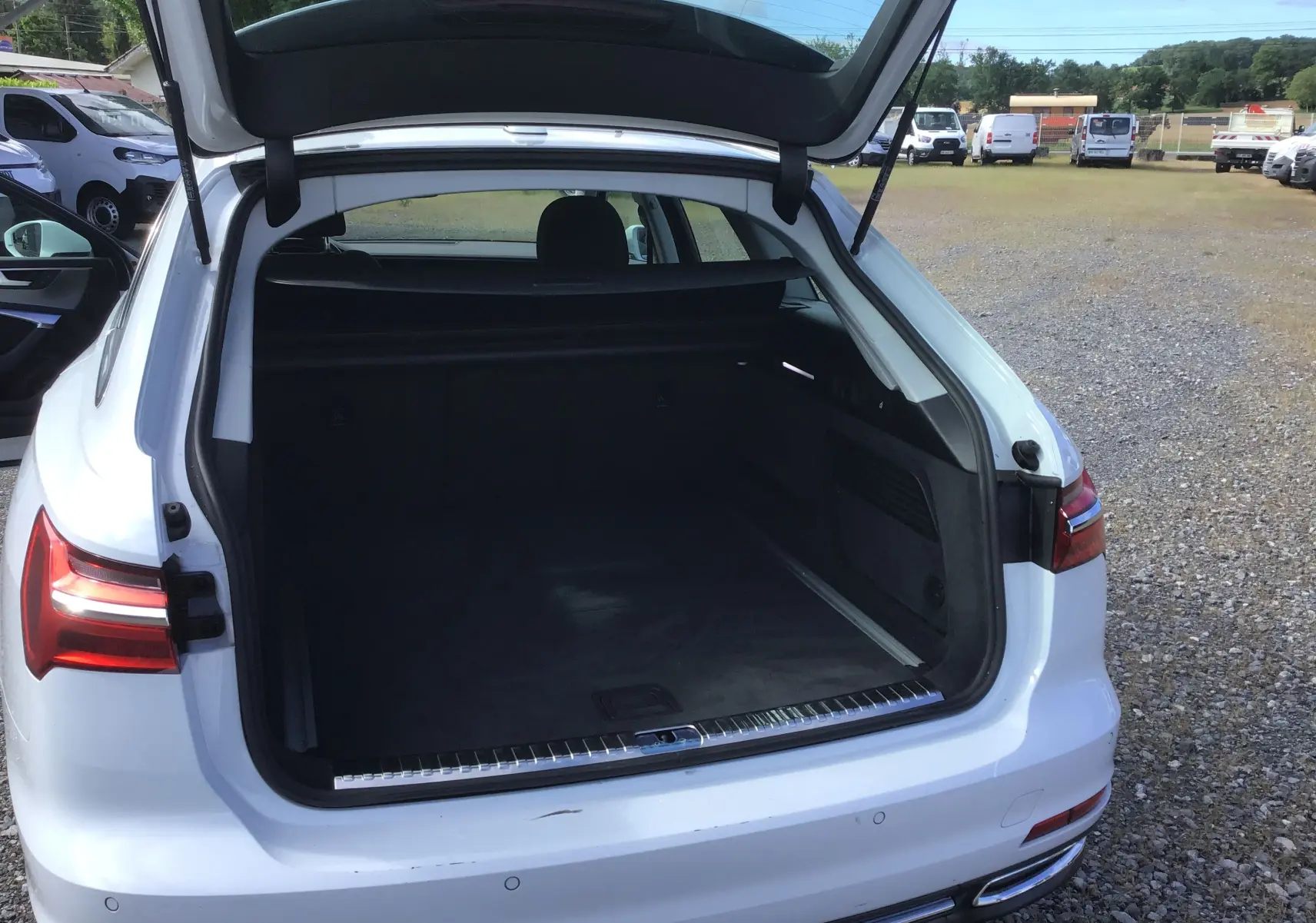 Coffre ouvert vu de l'arrière droit d'une Audi A6 Avant blanc glacier, avec intérieur de coffre spacieux et banquette arrière visible.