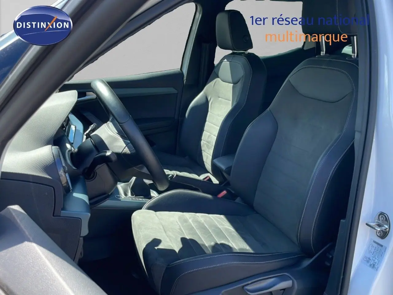 Vue intérieure côté conducteur du SEAT Arona blanc alpin avec sièges en cuir et alcantara noirs, volant multifonction visible.