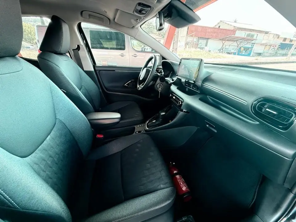 Intérieur avant droit de la Toyota Yaris Hybrid 116ch 2025, sièges noirs et tableau de bord moderne avec écran tactile.