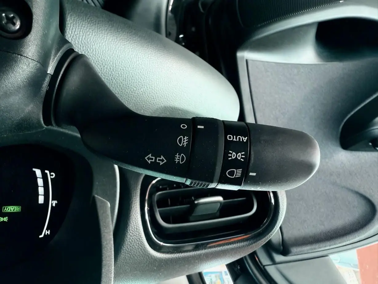 Gros plan sur la manette des feux et clignotants à gauche du volant dans l'habitacle noir d'une Toyota Yaris hybride 2025.